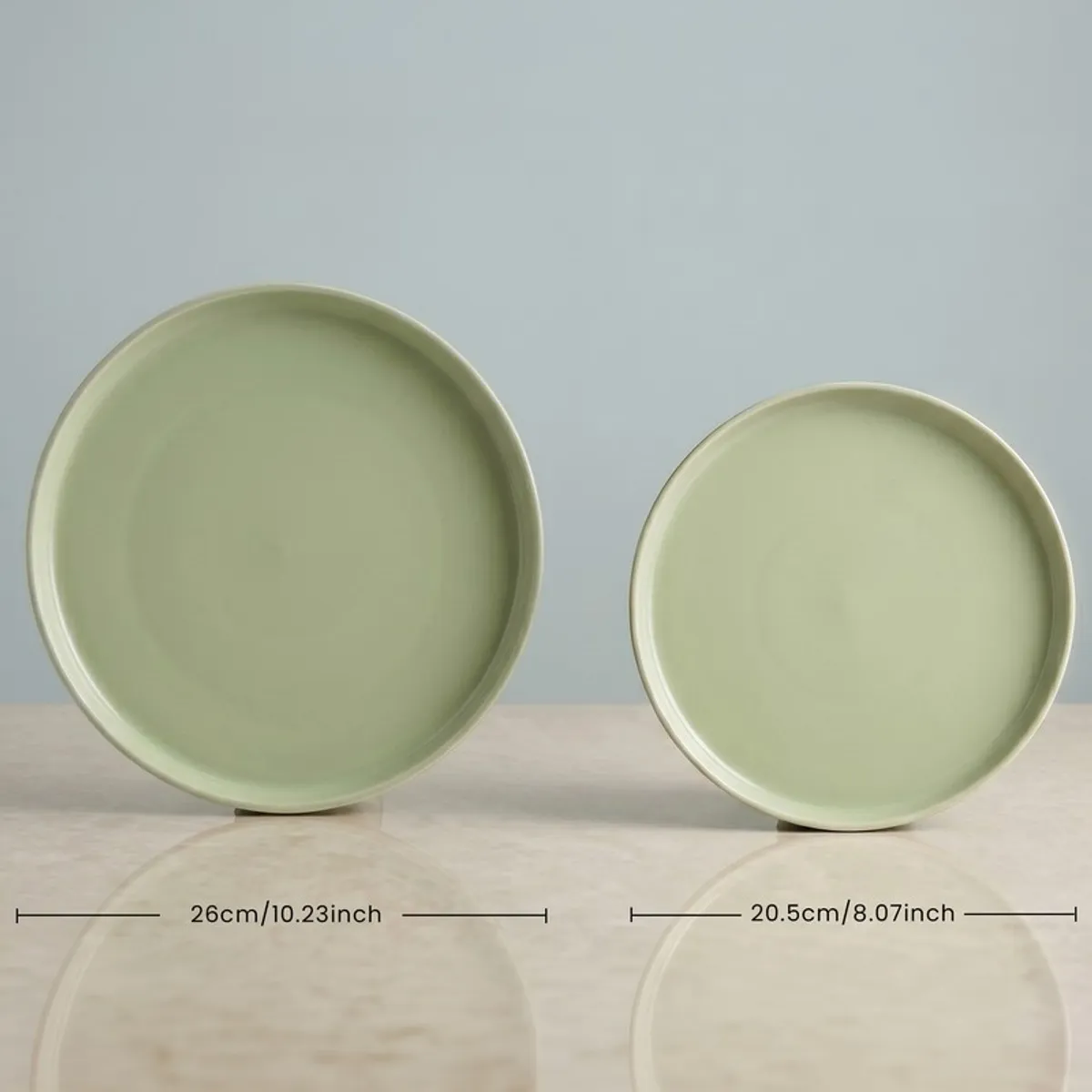Two round sage green plates displayed upright on a neutral surface