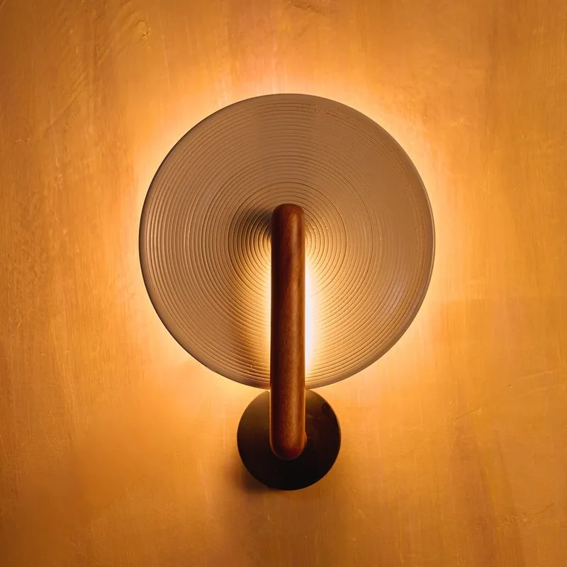 Centered view of glowing wall lamp with round ridged shade and wood arm