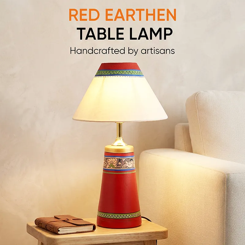 Red terracotta table lamp with cream shade styled beside a chair and book