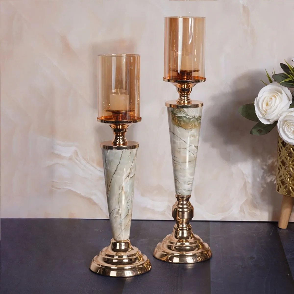 Two gold and white marble candle holders with glass shades beside white flowers