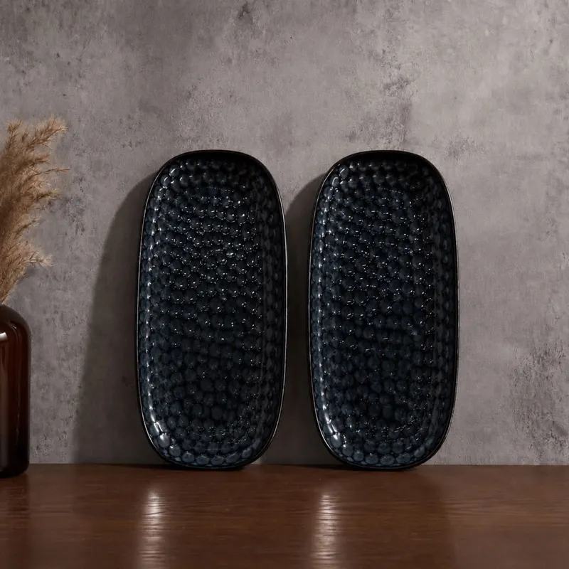 Two dark blue glossy textured oval platters displayed upright on a wooden surface