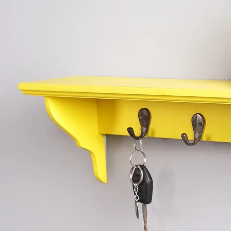 Close-up of yellow wooden shelf with dark metal hooks and hanging keys