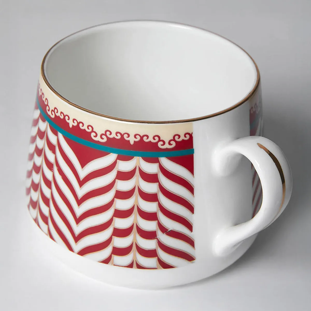 Close-up of a glossy white cup showing red chevrons, teal trim and handle