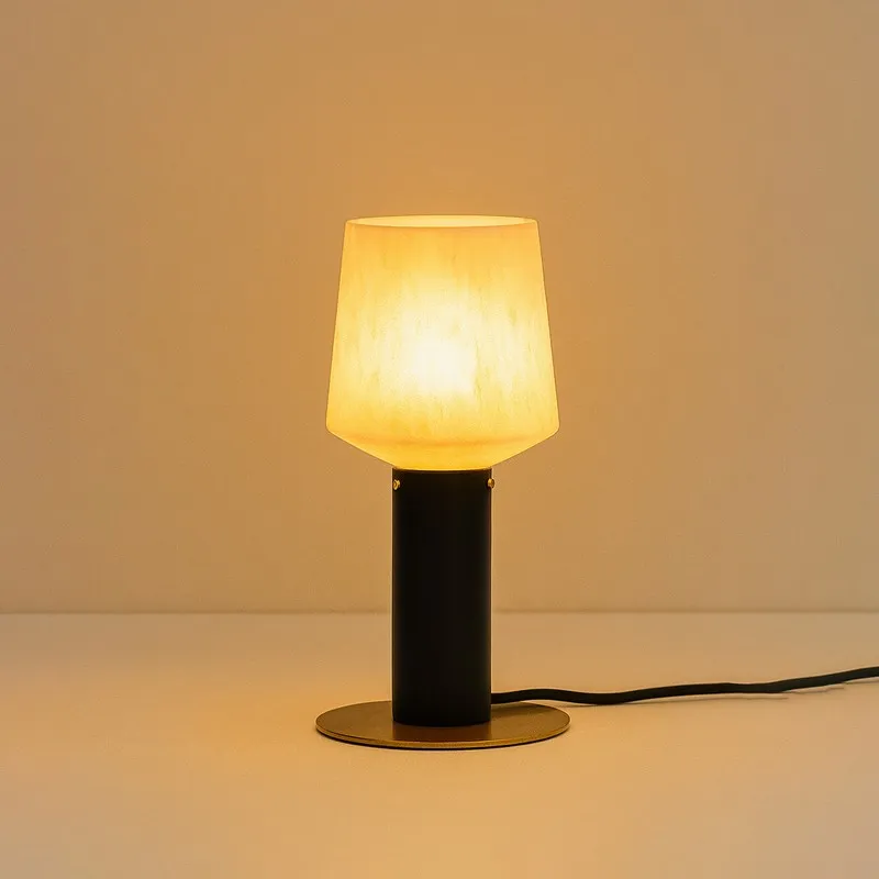 Black and off-white table lamp glowing warmly against a beige backdrop