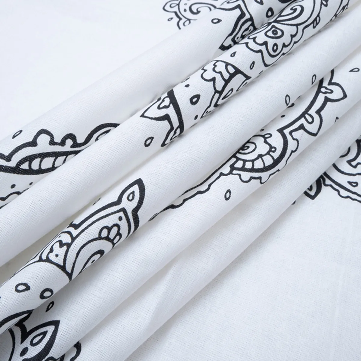 Folded white bedsheet showing black paisley detailing and soft fabric