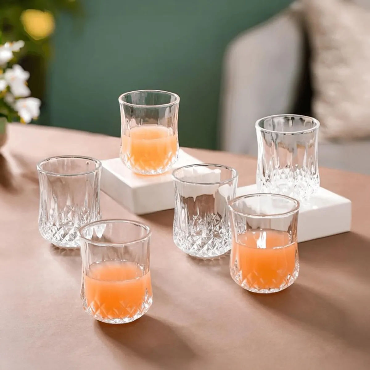 Six clear patterned glasses arranged on a table, some filled with orange juice