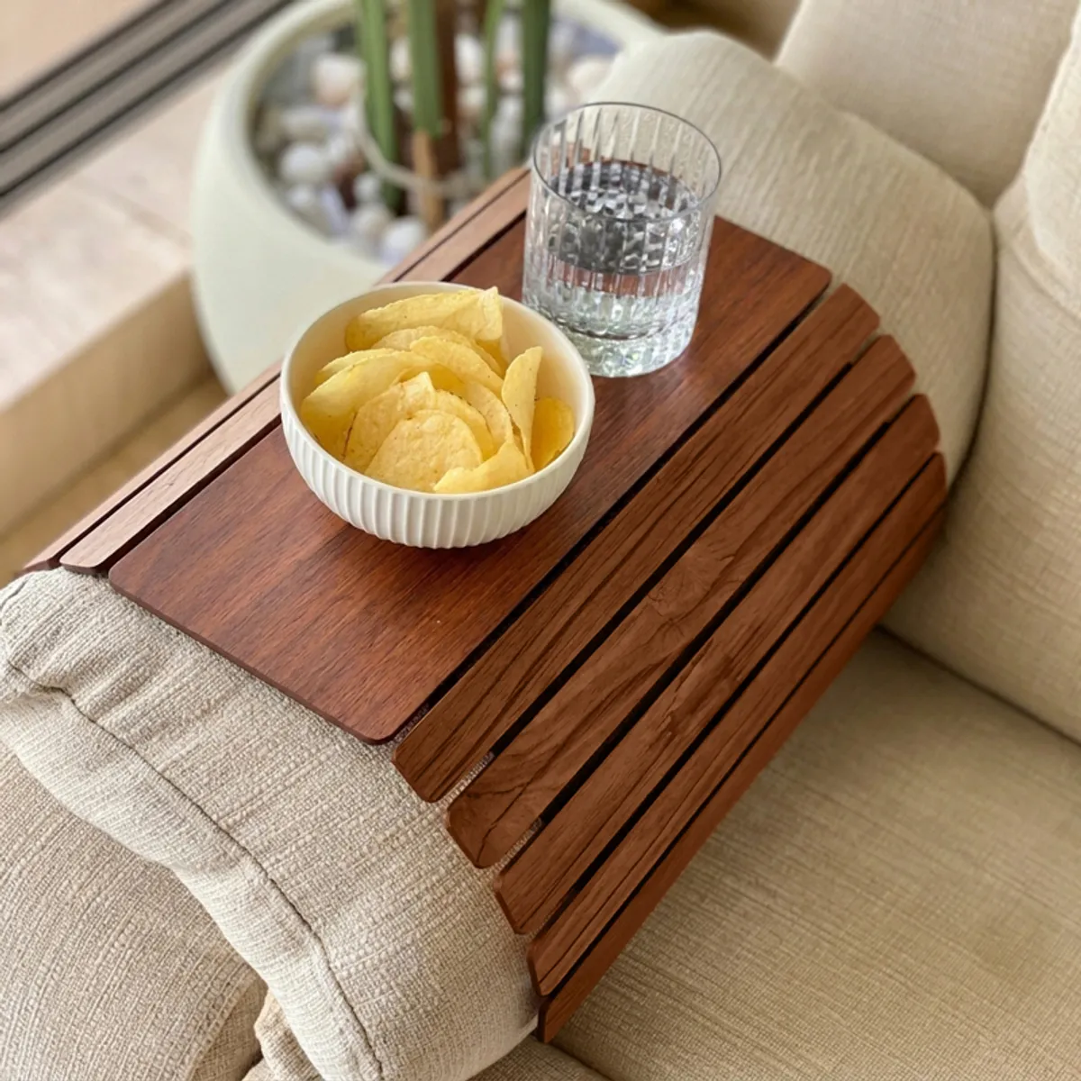 Close-up of brown slatted sofa armrest tray with snacks and drink