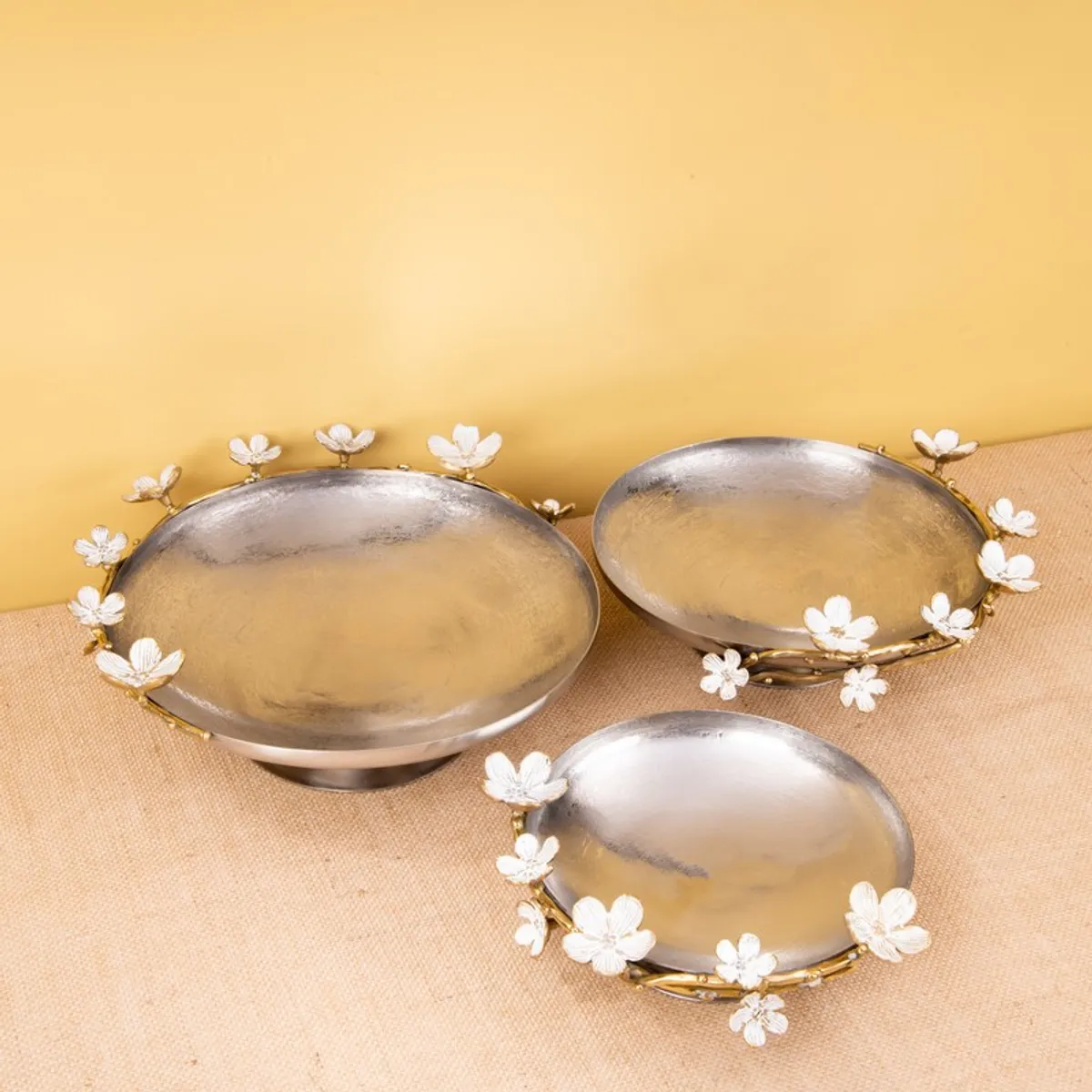 Three silver and gold floral accent bowls styled on a warm tabletop