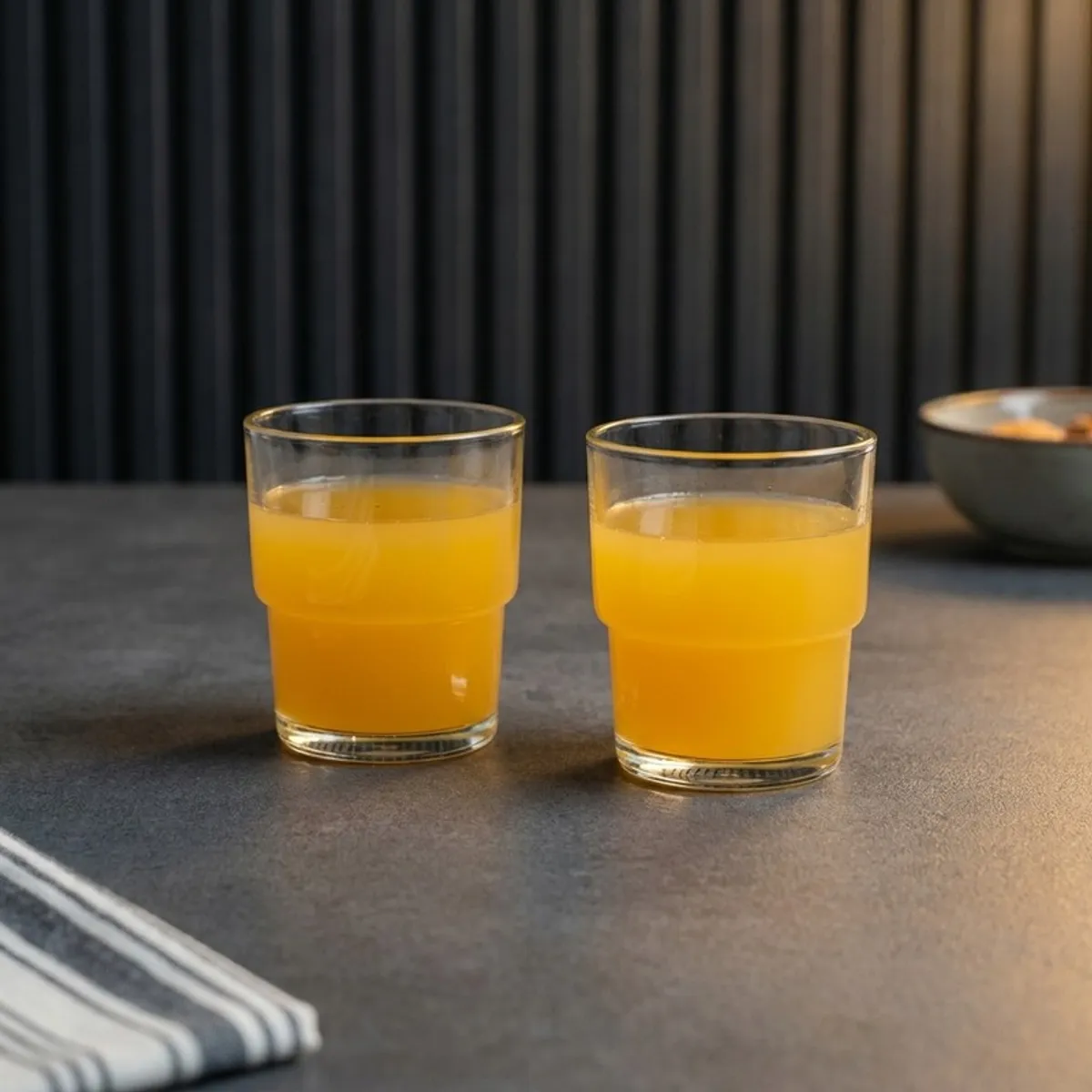 Two clear glasses filled with orange juice on a dark tabletop