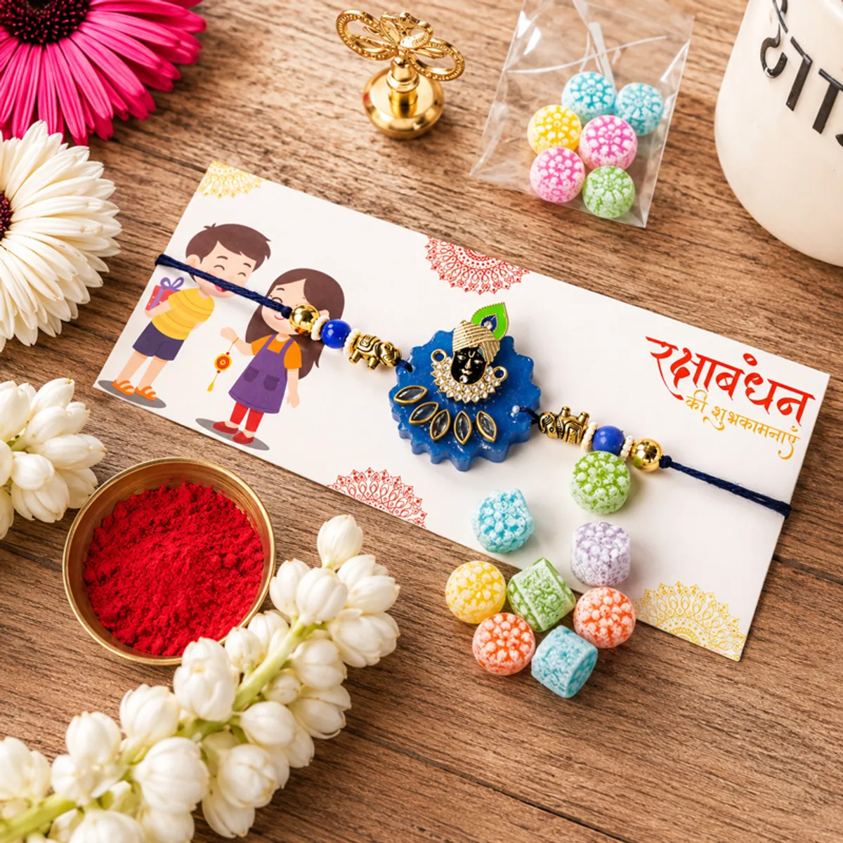 Decorative Krishna rakhi with colourful sweets and festive cards on a wooden surface