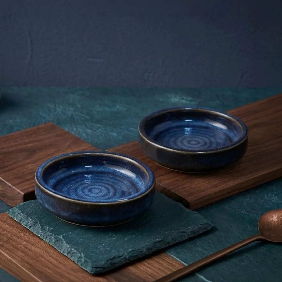 Two blue ceramic dip bowls with concentric interiors on serving boards
