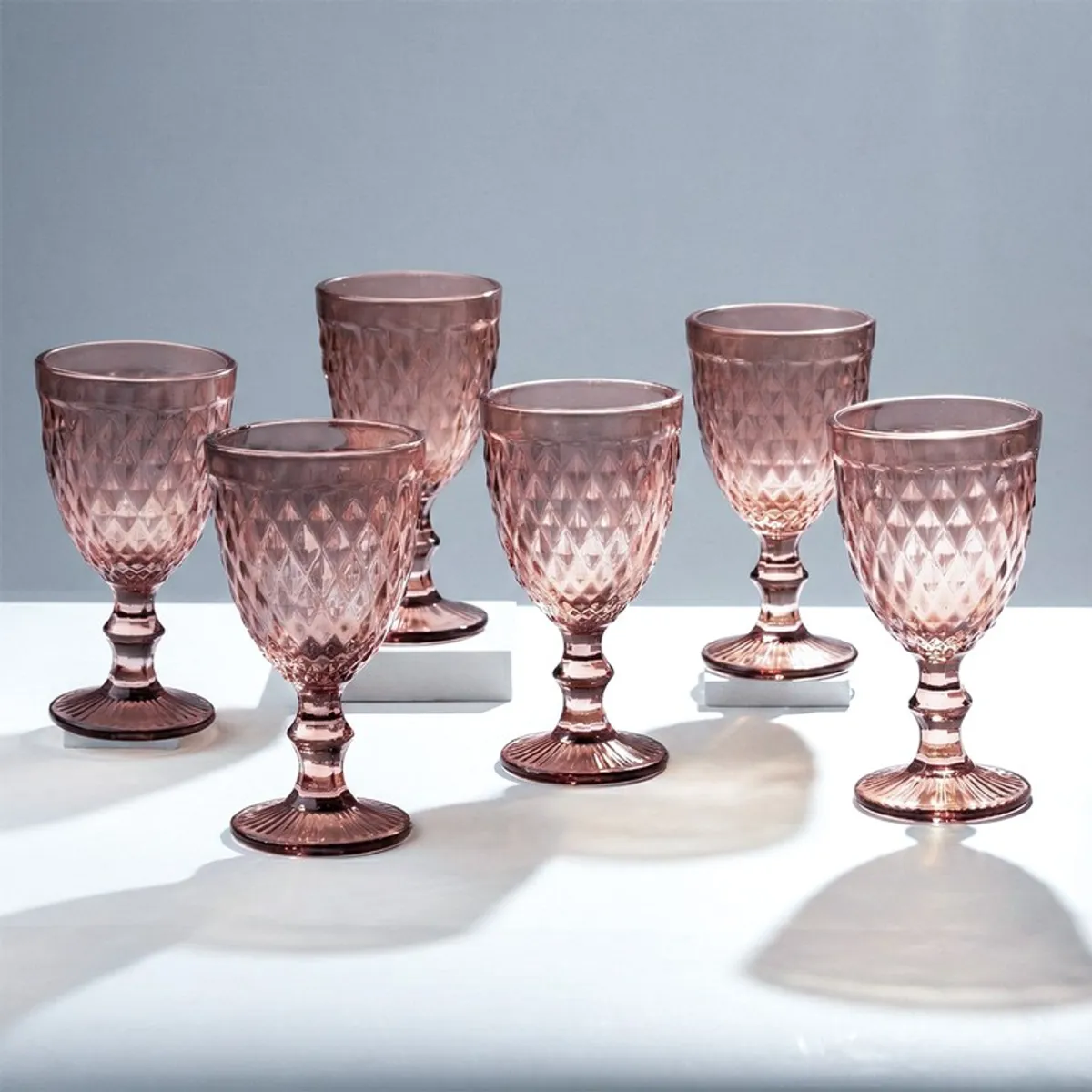 Five pink textured stemmed wine glasses arranged on a white surface