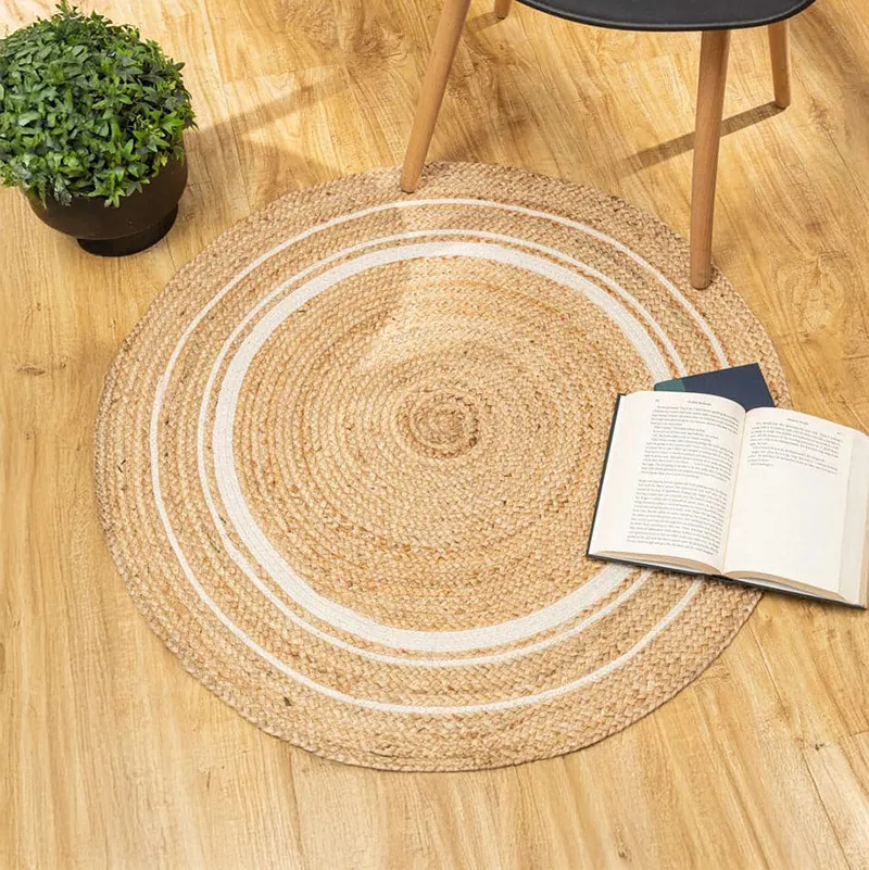 Round beige and white jute rug styled on a wooden floor with a chair and plant