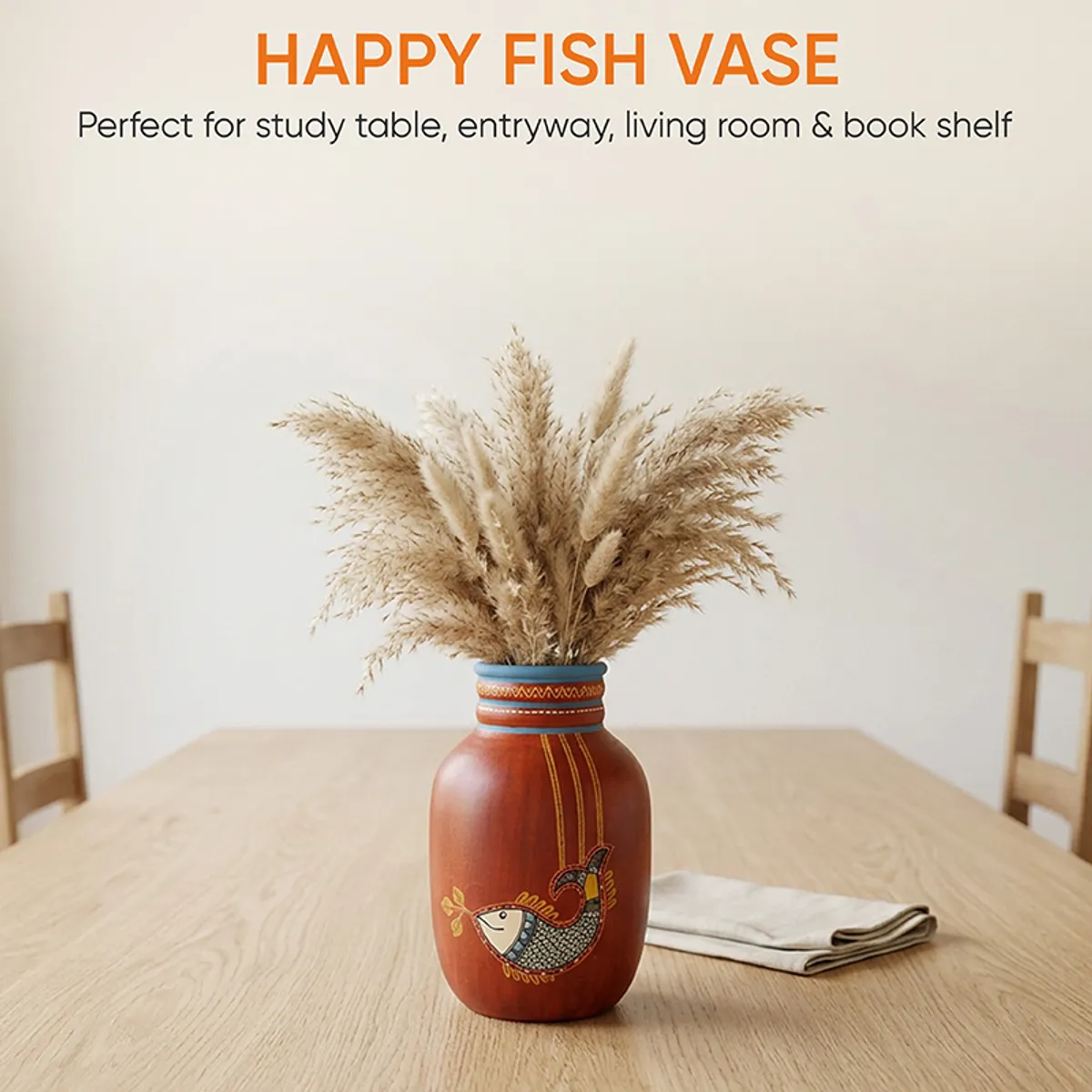 Red terracotta vase with dried grass placed at the centre of a wooden dining table.