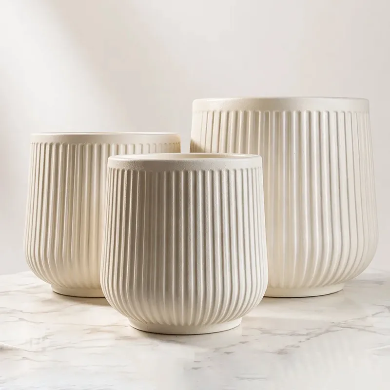 Three beige ribbed cylindrical planters displayed together on a marble surface.