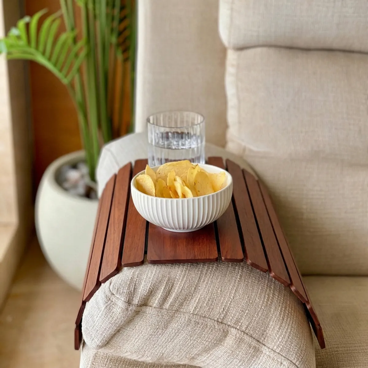 Brown sofa armrest tray holding a bowl of chips and glass