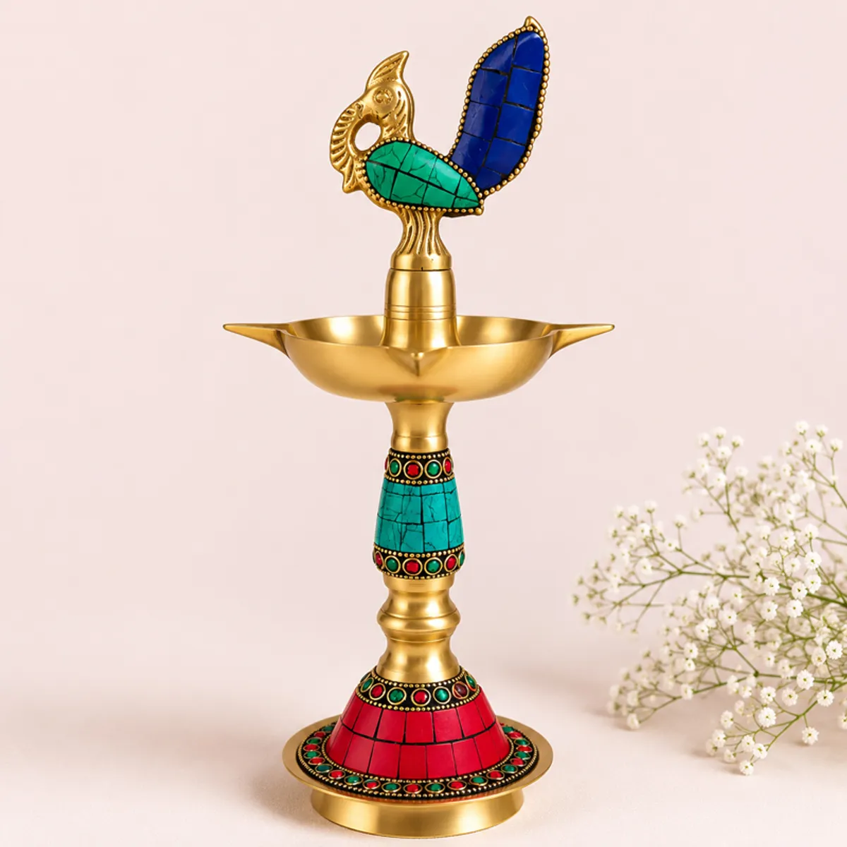 Single glossy brass diya with blue and teal peacock accents on a plain backdrop