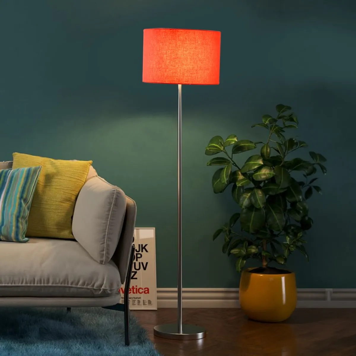 Lit orange drum shade floor lamp beside sofa and plant against a teal wall