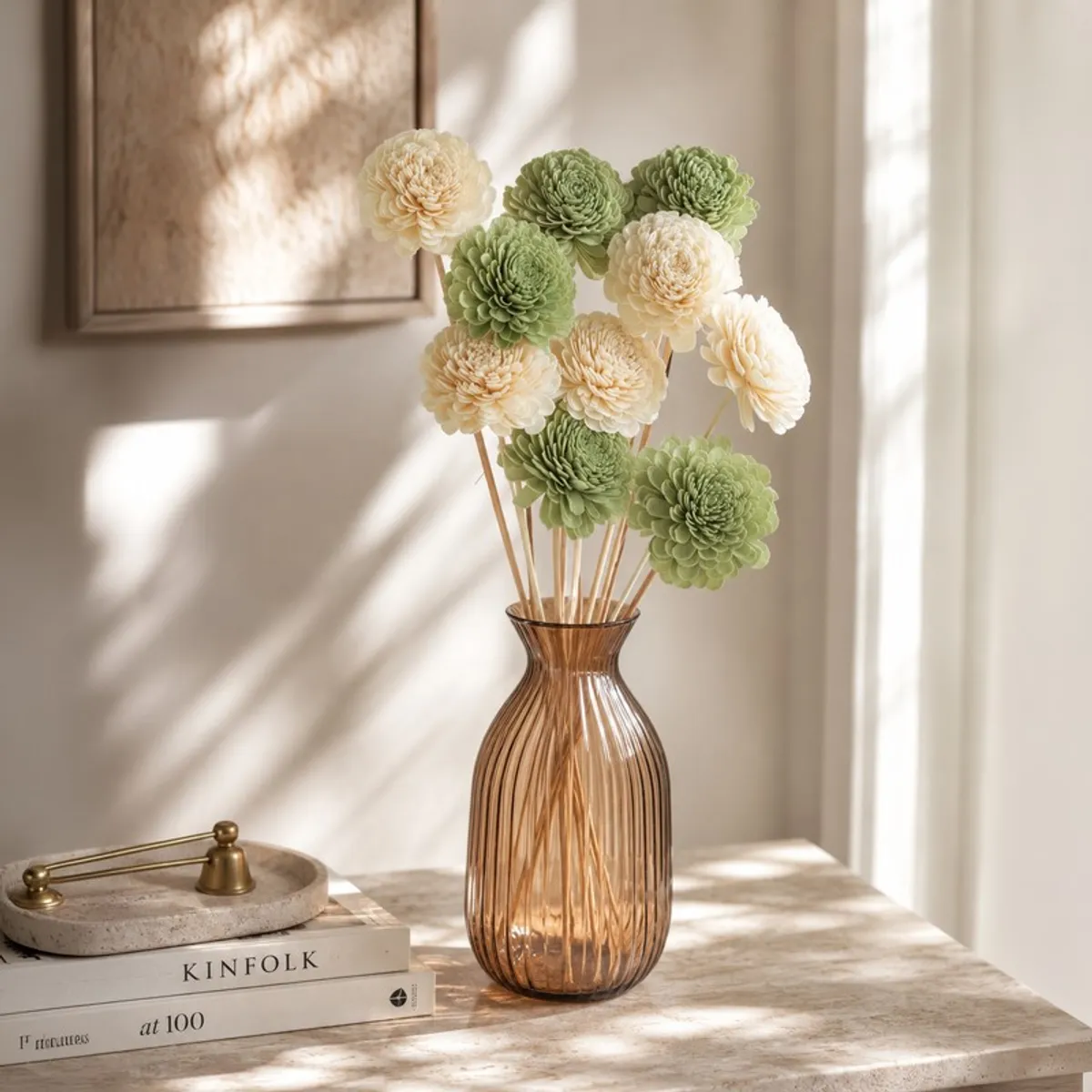 Green and off-white flower sticks displayed in an amber vase on a tabletop