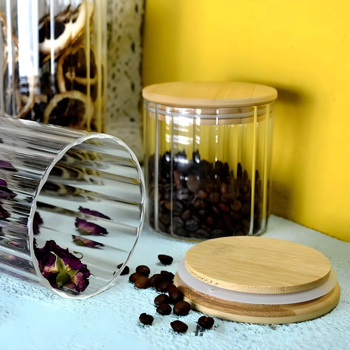 Fluted glass jar with bamboo lid displayed beside coffee beans and its open lid.