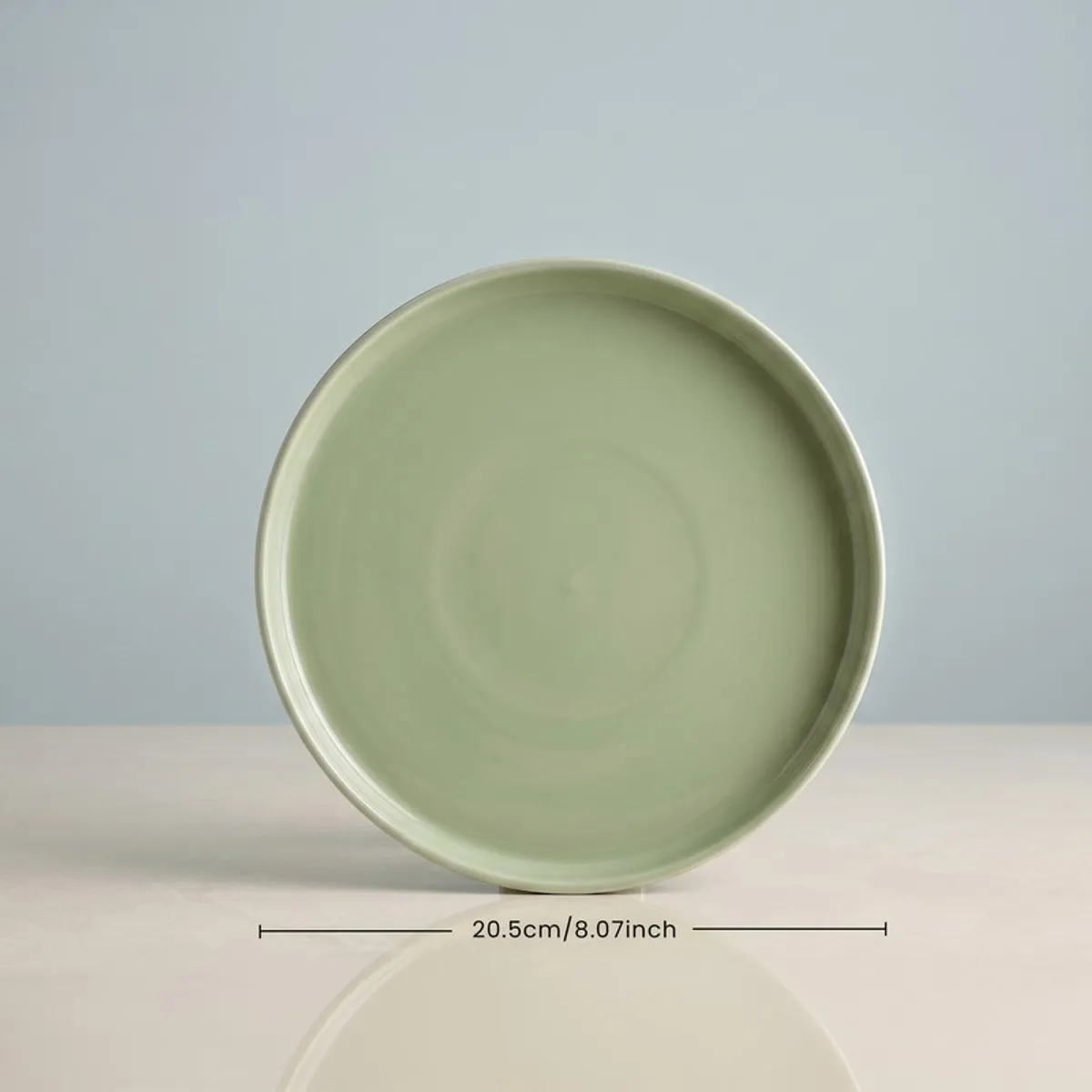 Single sage green round plate on display against a pale blue background