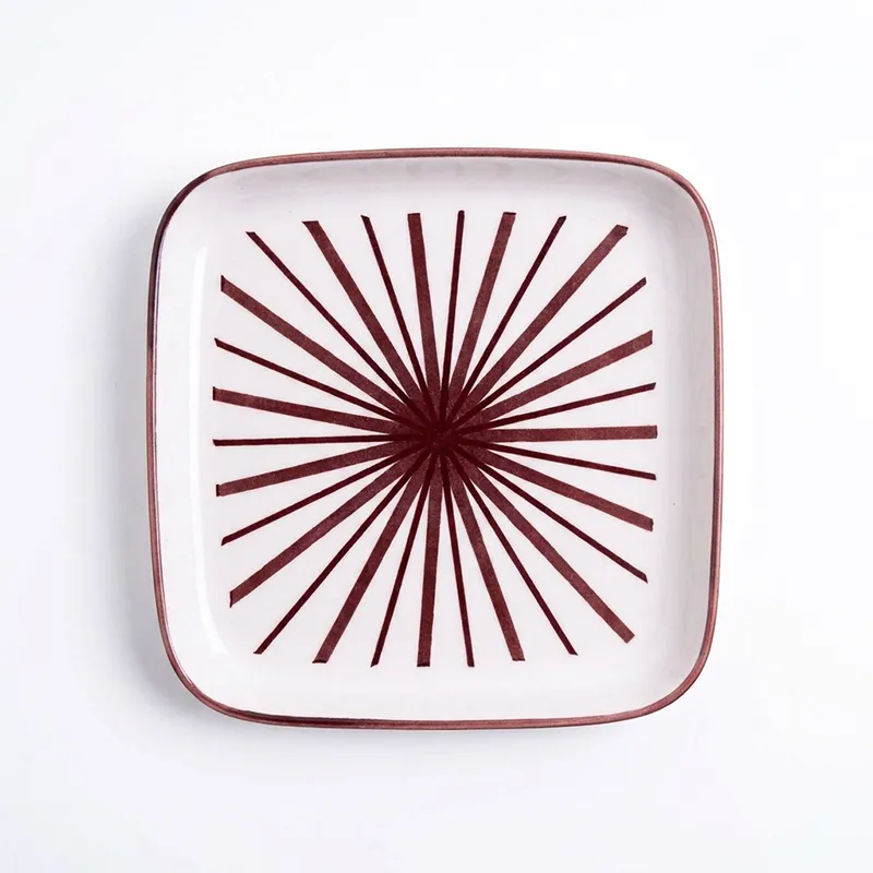 Top view of square white plate with maroon starburst motif