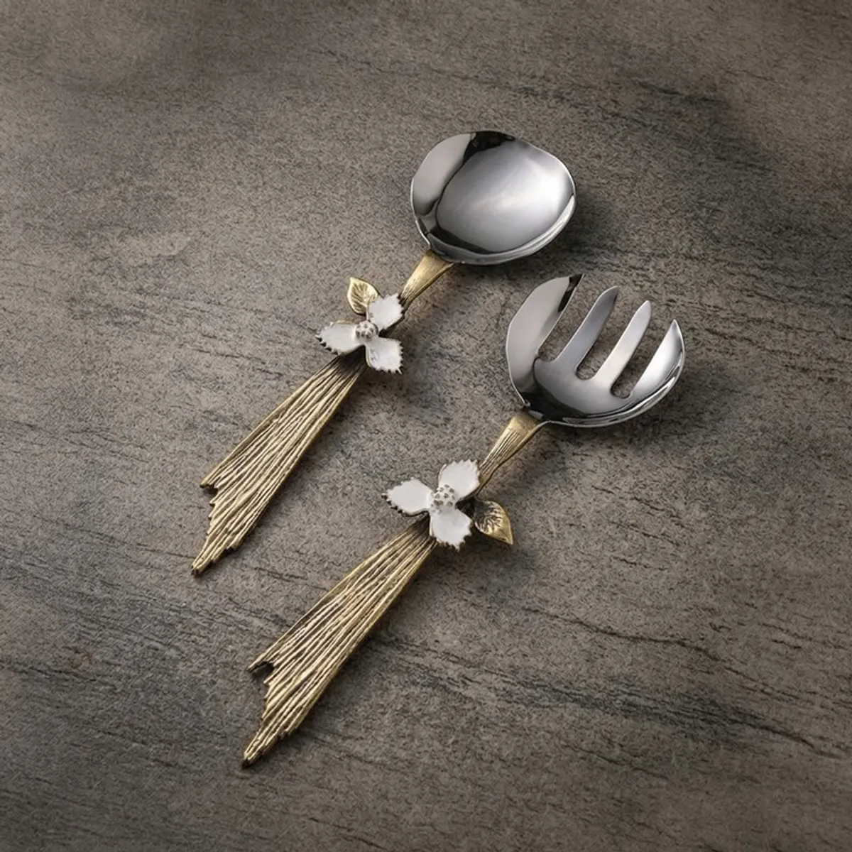 Silver and gold salad spoon and fork arranged on a grey textured surface