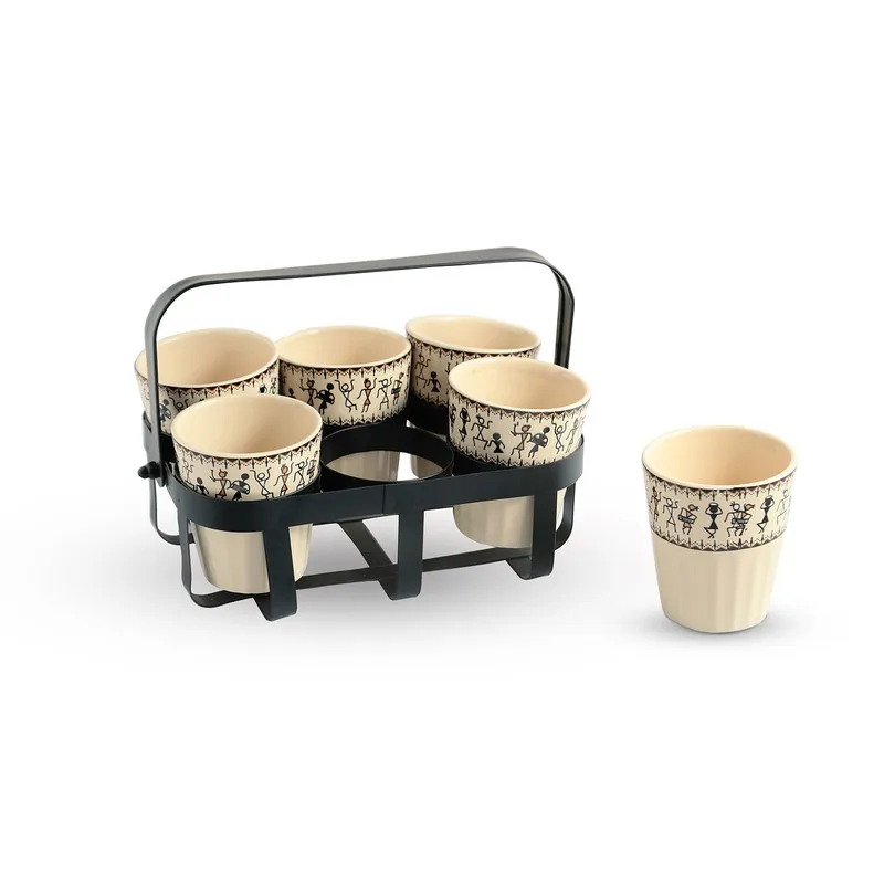 Six Warli-patterned tea cups displayed in a black holder with one cup beside it
