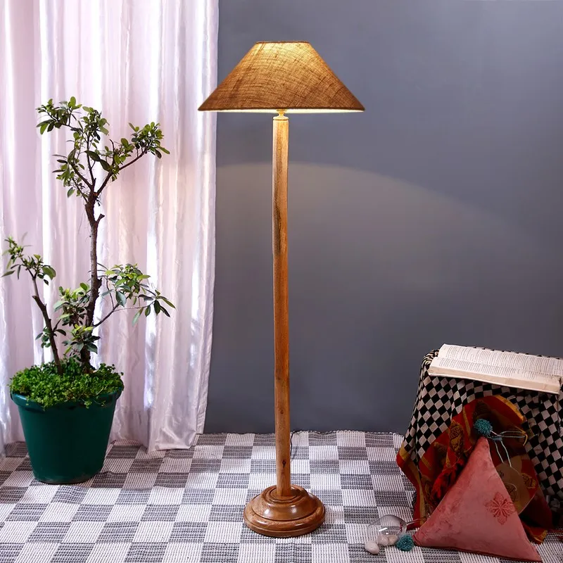 Wooden floor lamp with a brown shade styled beside a potted plant and draped table
