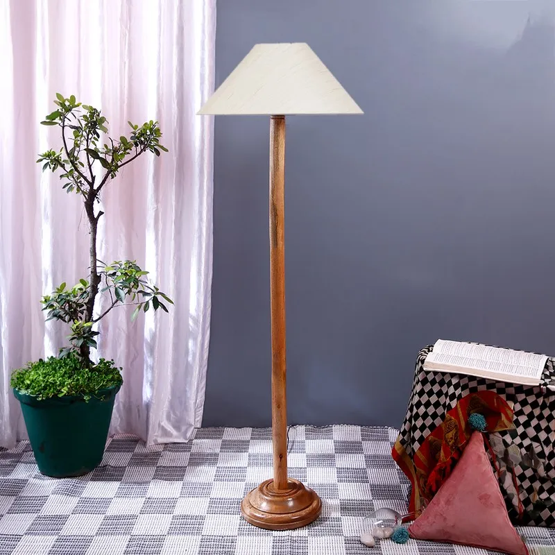 Wooden floor lamp with an off-white cone shade beside a potted plant and draped stool.