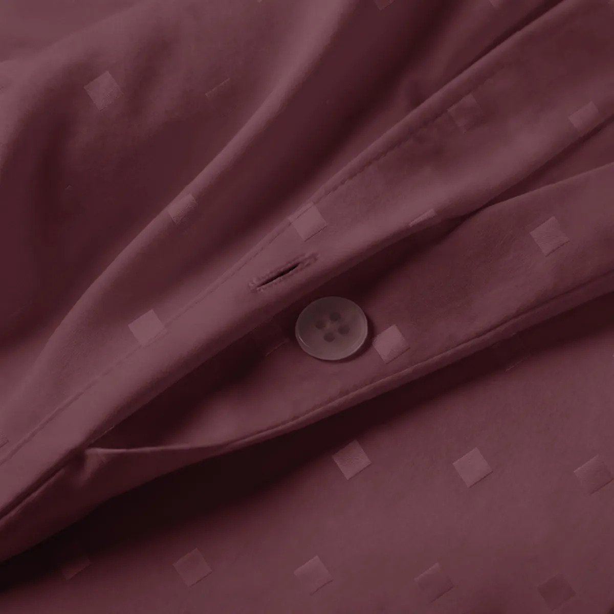 Close-up of maroon duvet cover fabric with subtle square dot texture and button closure