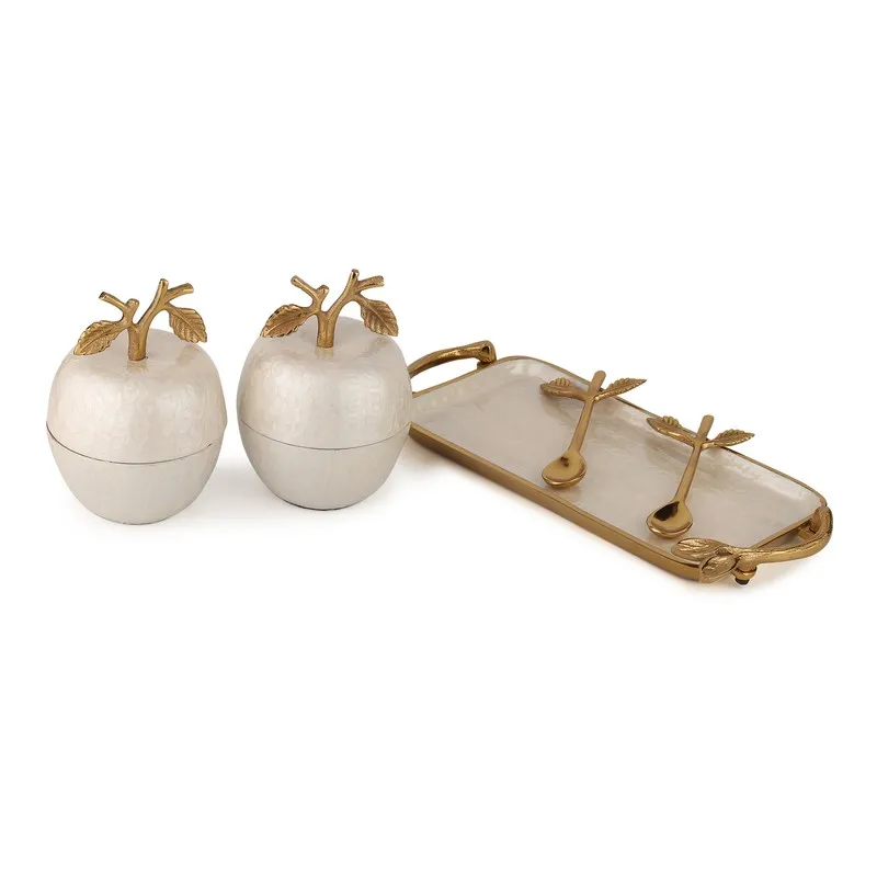 Two ivory apple jars beside a gold-trimmed tray with decorative spoons