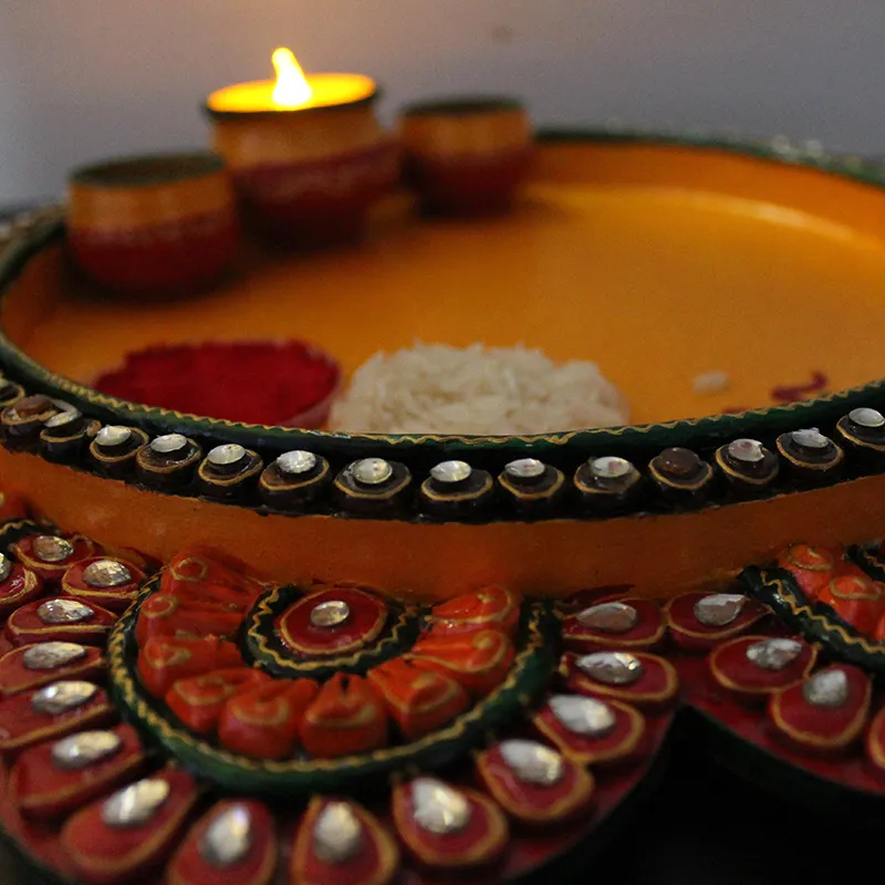 Close-up of textured yellow pooja plate with embellished floral edge and bowls