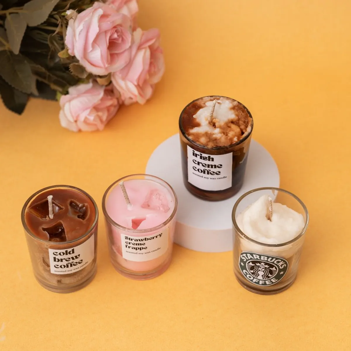 Three colourful jar candles arranged around a raised white display stand.