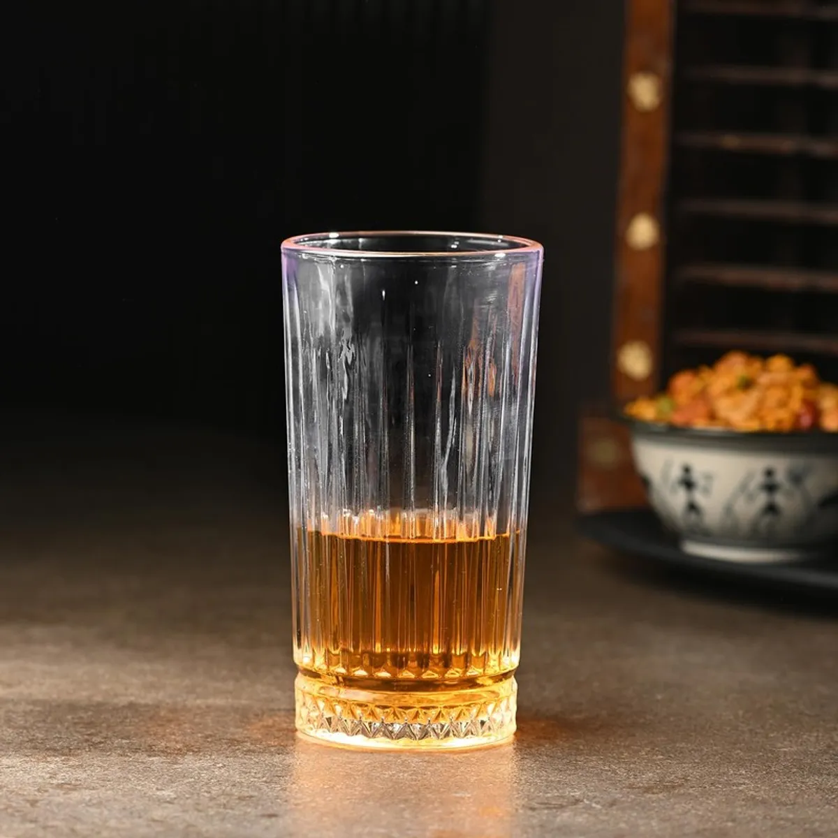 Single clear textured drinking glass partly filled with amber drink