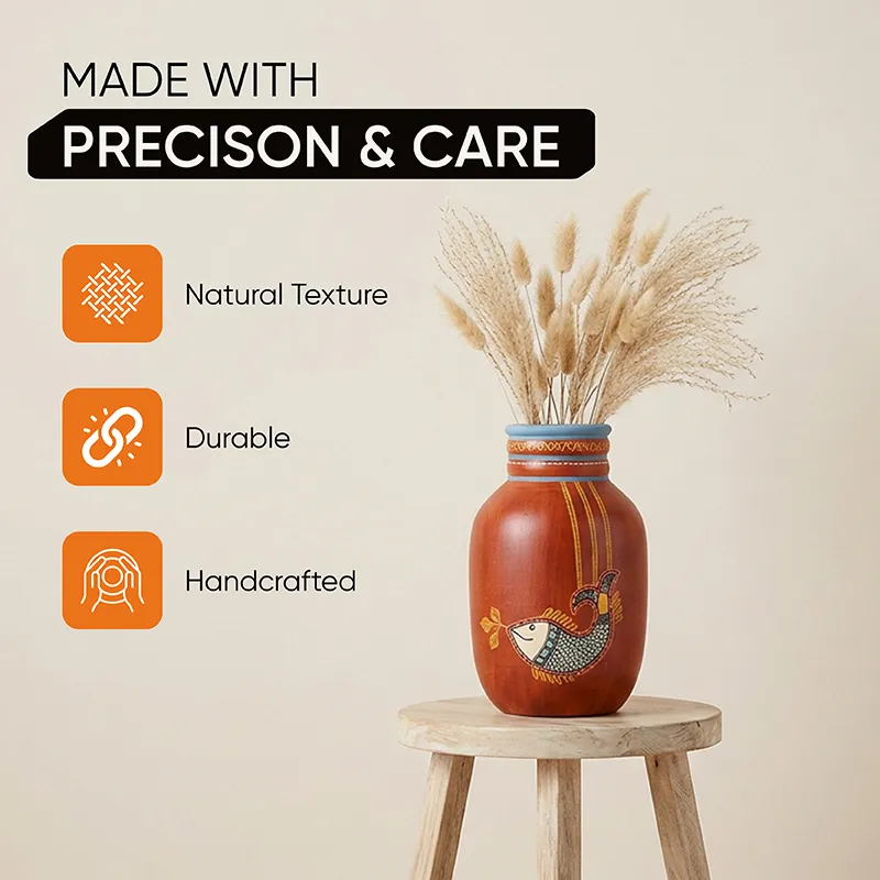 Red fish motif vase with dried stems placed on a round wooden stool indoors.