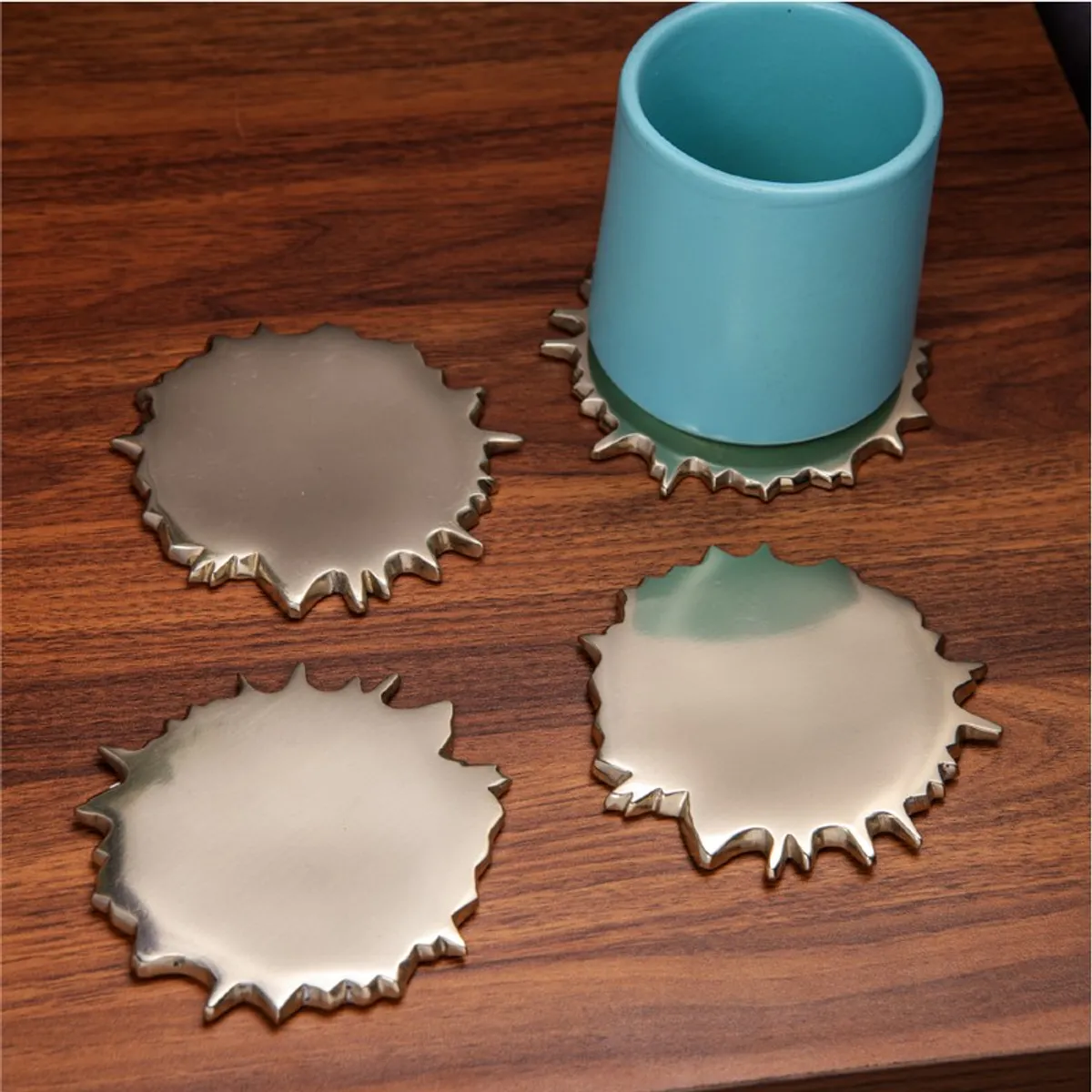 Four gold spill-shaped coasters with a blue cup on a wooden surface