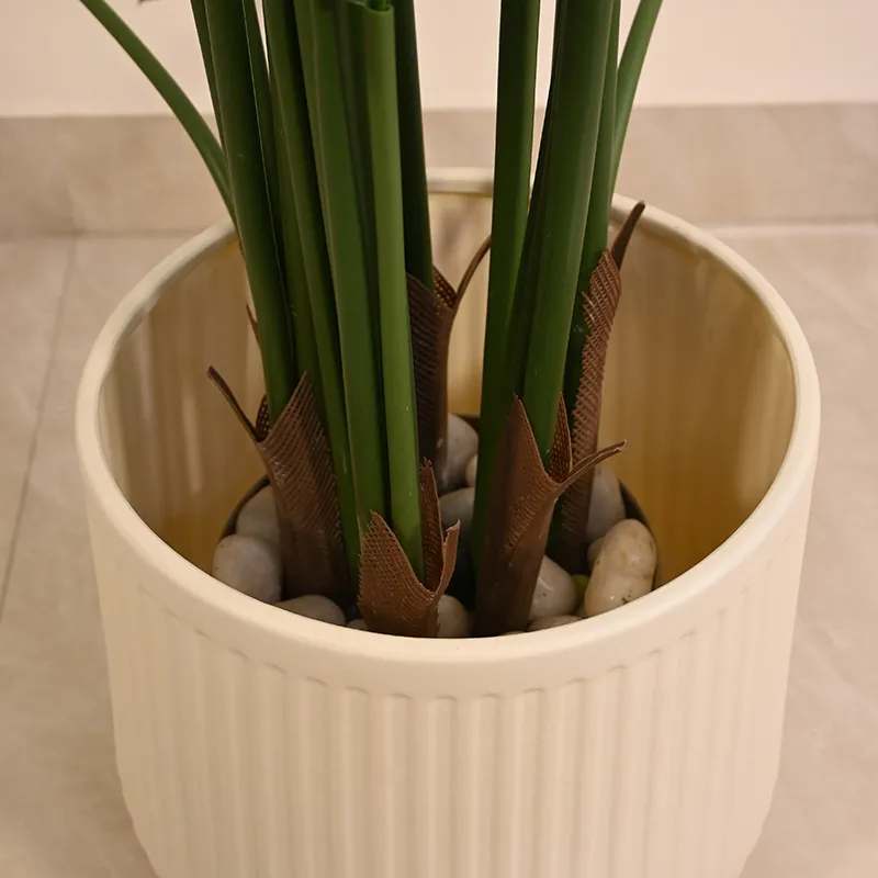 Close-up of a beige ribbed planter holding green plant stems and decorative stones.