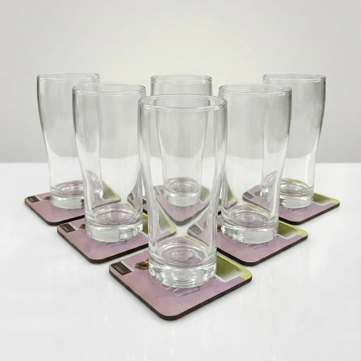 Six clear cylindrical drinking glasses arranged together on square coasters