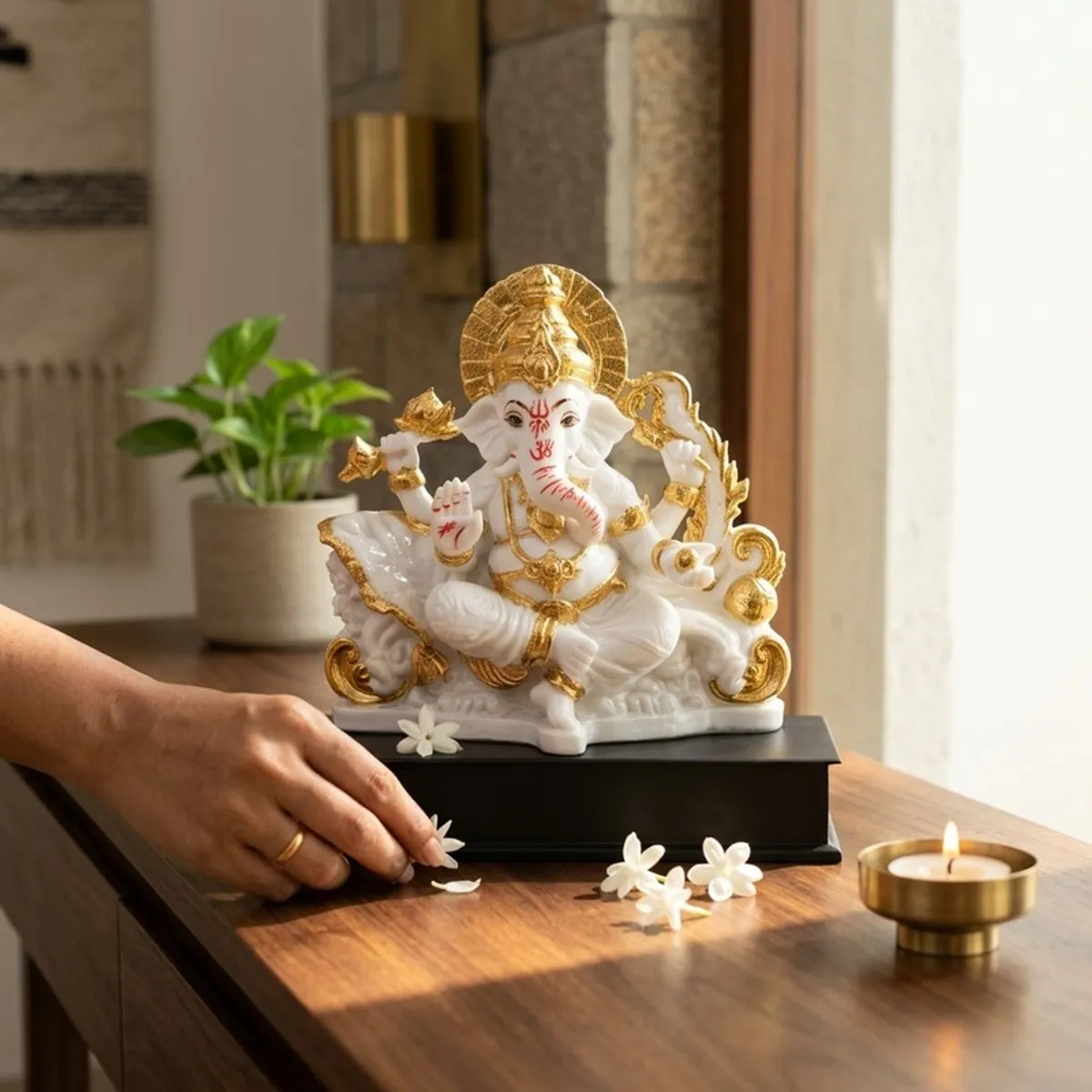 White and gold Ganesha idol styled on a tabletop with flowers and a lamp
