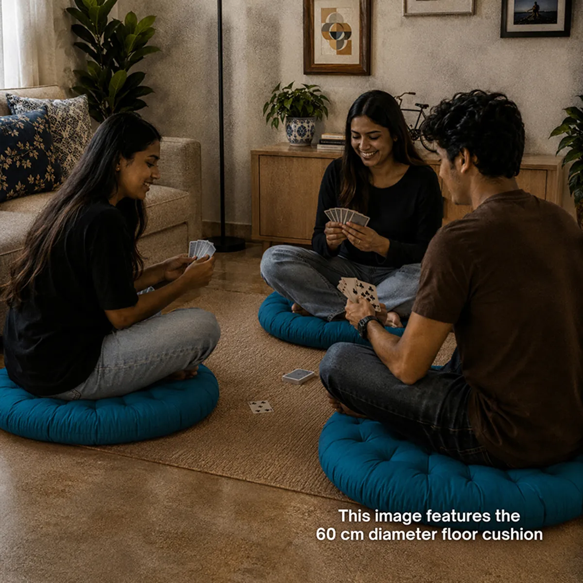 Three people seated on round deep green floor cushions while playing cards indoors