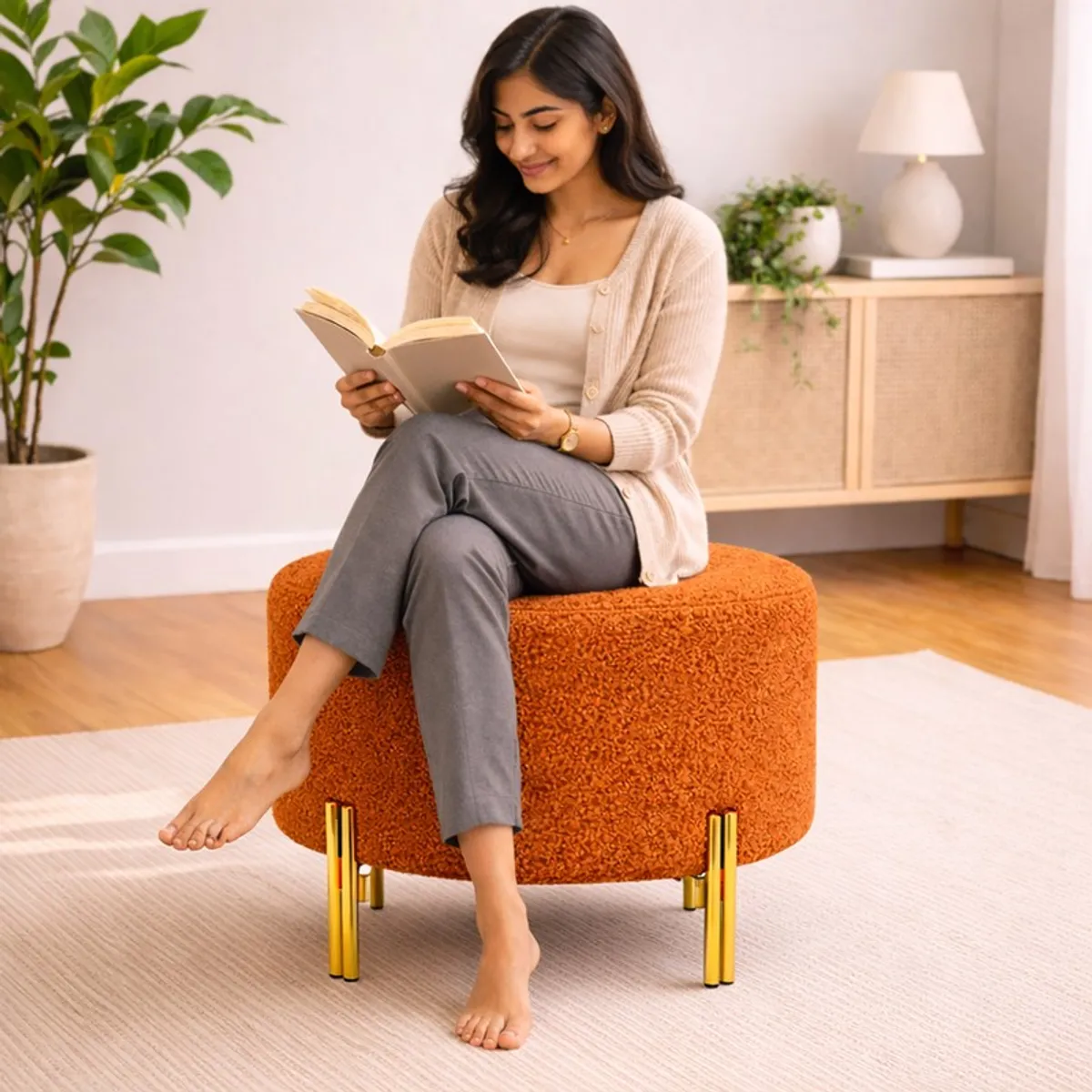 Person seated on a round orange boucle ottoman with gold legs