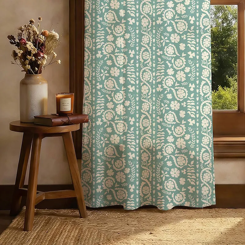 Green floral printed curtain panel hanging beside a wooden window and side table