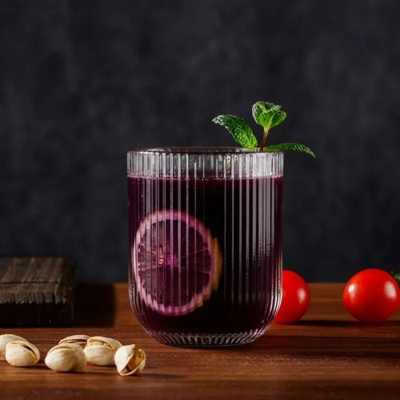 Clear cylindrical glass with vertical lined detailing holding a dark drink and mint garnish