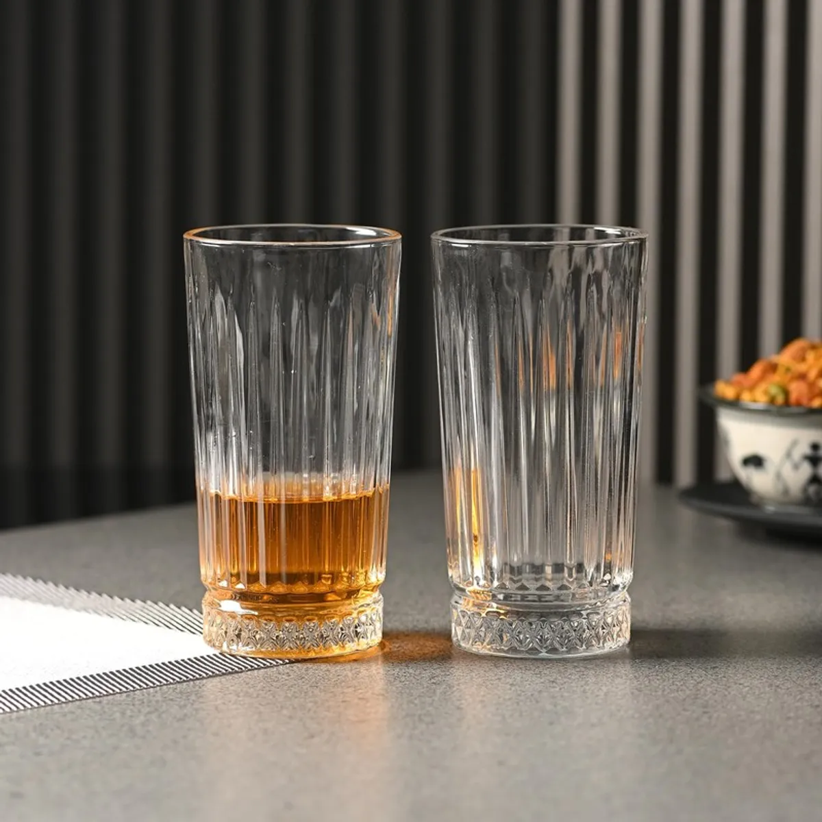 Two clear textured drinking glasses, one partly filled with amber drink