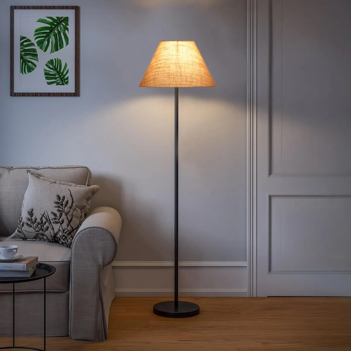 Lit beige jute floor lamp with black stand beside a sofa