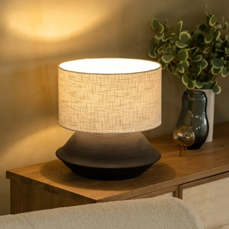 Black ribbed table lamp with beige shade styled on a wooden sideboard
