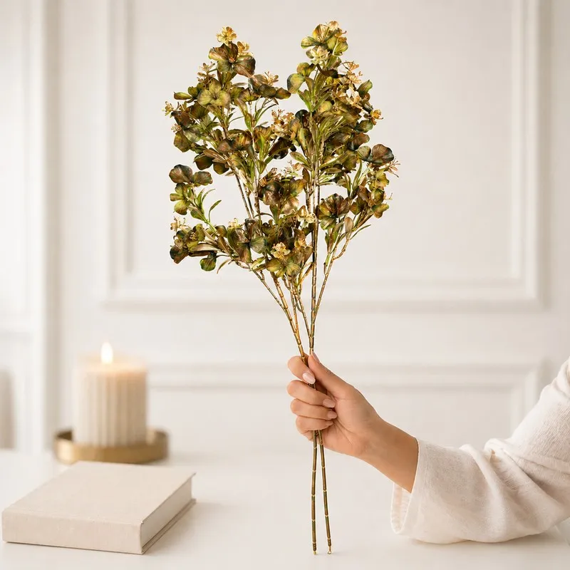 Hand holding two artificial flower stems with green and yellow blooms
