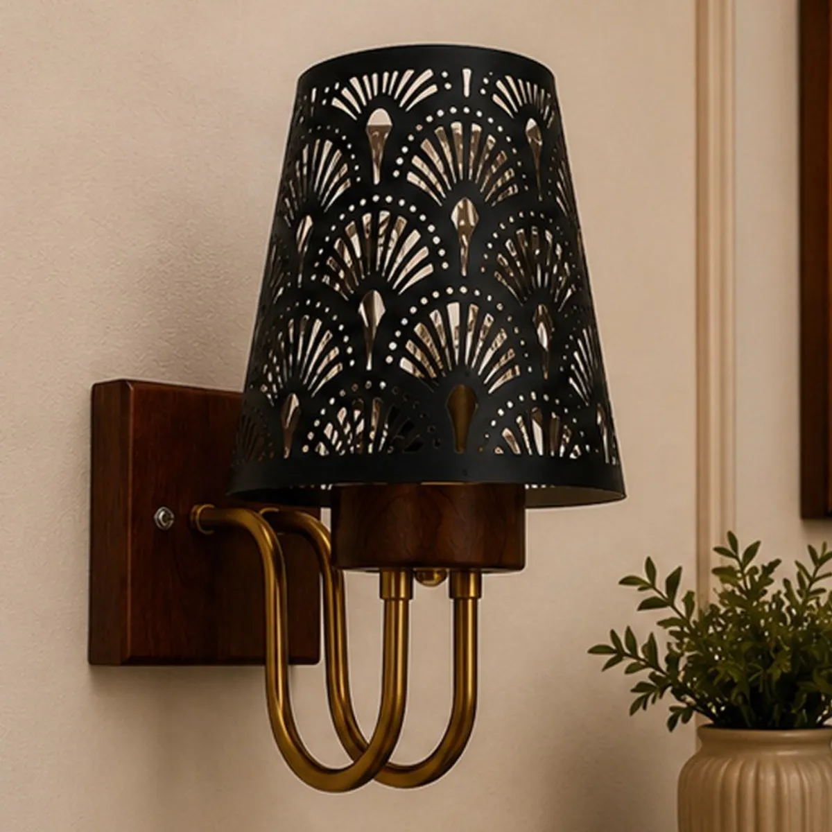 Close-up of a black patterned shade, wood mount and gold-toned curved arms on a wall.