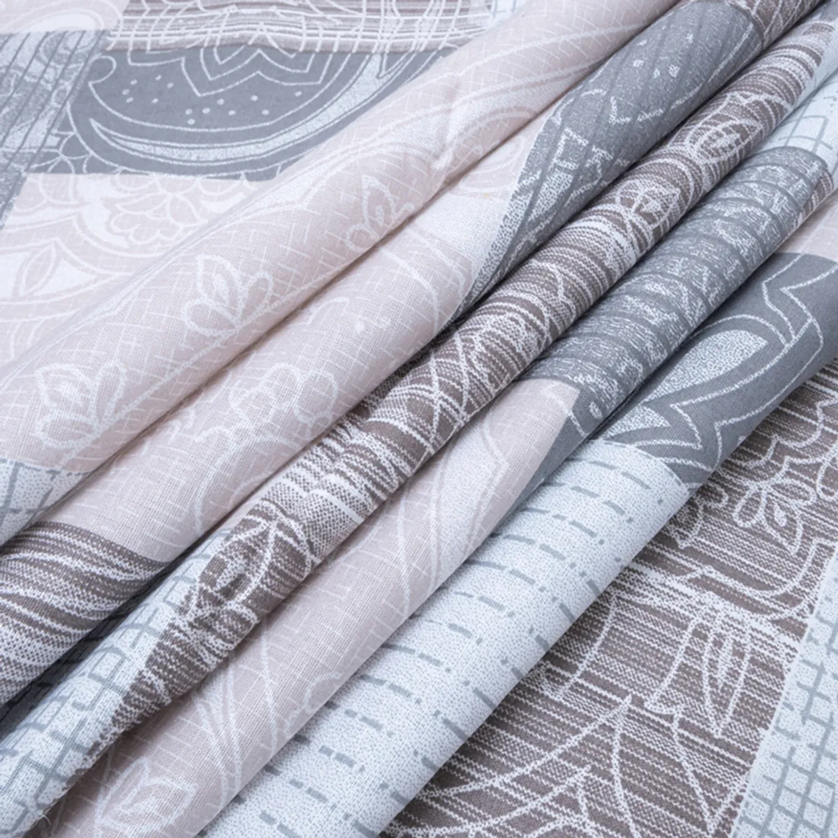 Folded bedsheet fabric showing soft grey, beige and off-white geometric print